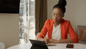 Young adult african american woman is studying using a video call - noting down the lesson. Distant education and skill share