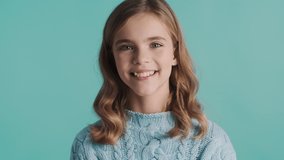Pretty blond teenager girl with wavy hair looking sly thinking on camera and smiling over blue background