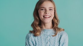 Funny blond teenager girl smiling showing tongue on camera and after it looking serious isolated on blue background