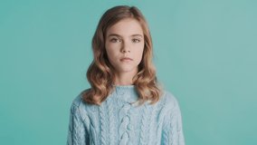 Blond teenage girl shrugs shoulders showing I don't know gesture on camera isolated on blue background. Human reaction concept