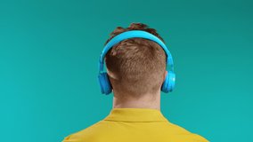 Unrecognizable man listening to music with headphones, guy dancing in studio on blue background. Wireless technology, radio concept.
