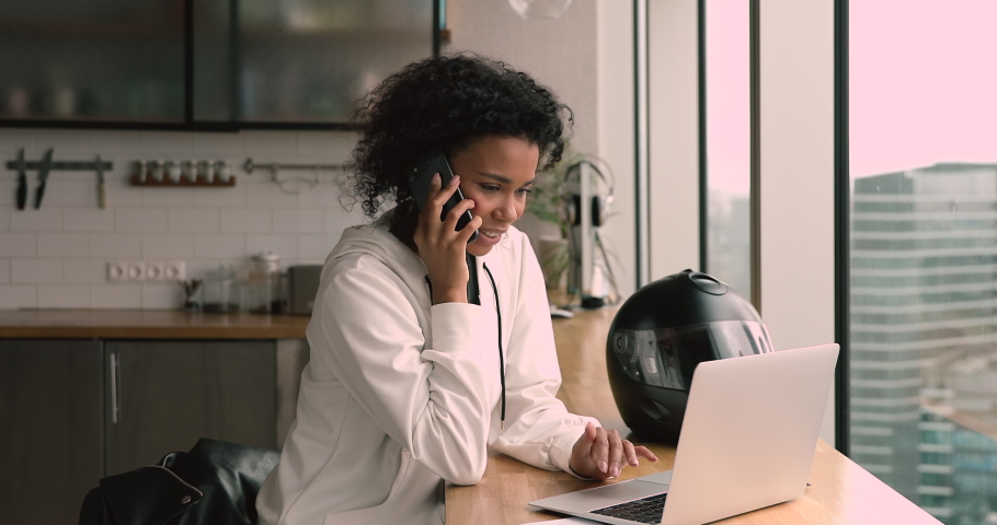 Happy young african american businesswoman holding mobile phone call while working on computer in modern office, female biracial freelancer making online order or communicating with client distantly. Royalty-Free Stock Footage #1068545114