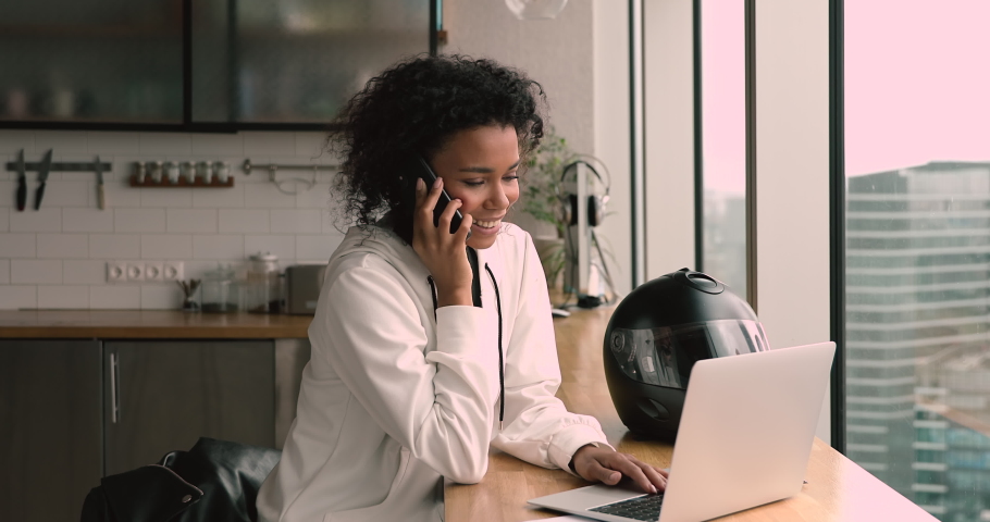Happy young african american businesswoman holding mobile phone call while working on computer in modern office, female biracial freelancer making online order or communicating with client distantly. | Shutterstock HD Video #1068545114