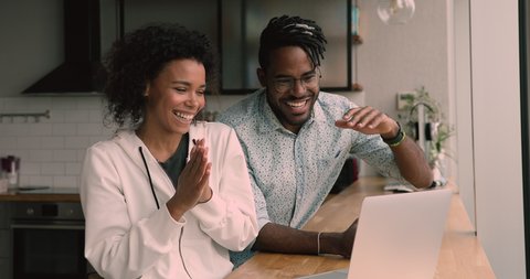 Happy young african mixed race family couple looking at computer screen, amazed by reading email with good news, finding good sale profitable shopping deal, feeling excited giving high five at home.