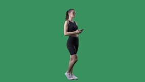Young active fit woman streaming selfie videos greeting with smartphone. Full body on green screen chroma key background. 