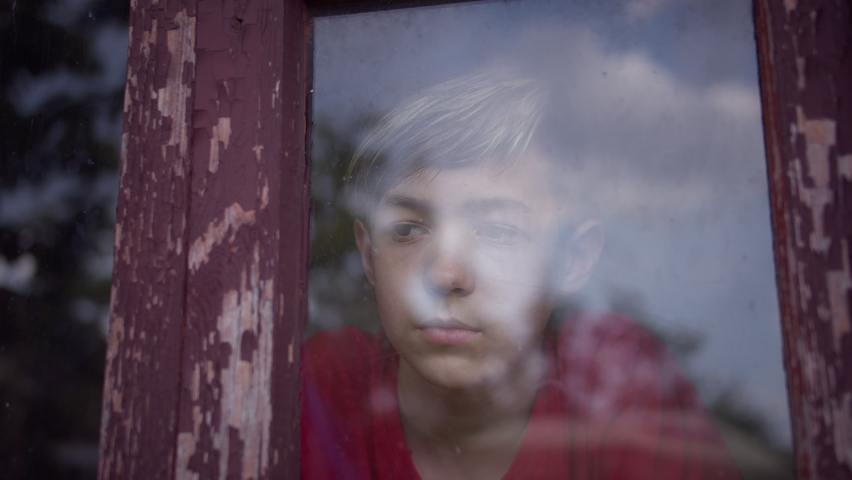 serious sad boy looks out the old shabby window and thinking about something