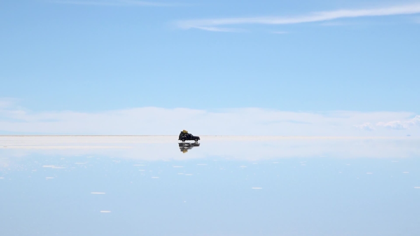 Panorama of Uyuni Salt Flats in Bolivia. Salt flat desert is covered by water in wet season. Reflections of cars and mountains at big distance.