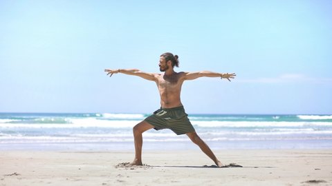 Young attractive millennial man practice yoga pose on the beach. Confident fit yogi guy. Concept of wellbeing, healthy balanced lifestyle. 