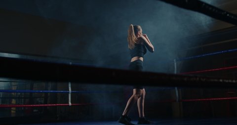 Athletic female boxer training hard in boxing ring, punching with fists, striking hard and fast. Muscular young woman practicing self-defence techniche.