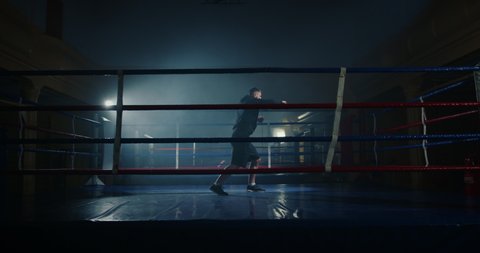 Cinematic shot of determined man athlete training hard striking on boxing ring, practicing fight moves. Professional boxer getting ready for kickboxing competition.