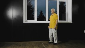 Old man athlete performs movement in a rack by the window