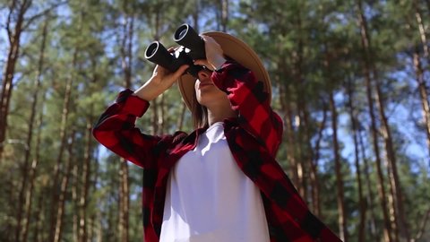 Girl in a hat looks through binoculars in the forest. Concept hike, tourism.
