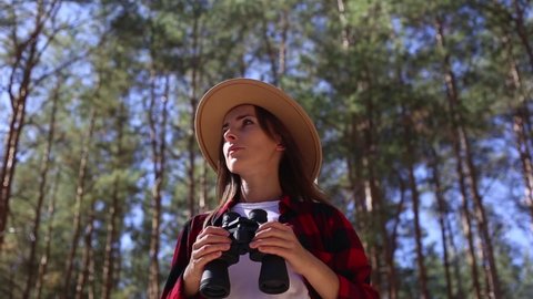 Woman in a hat holds binoculars while hiking in forest. Concept hike, tourism.
