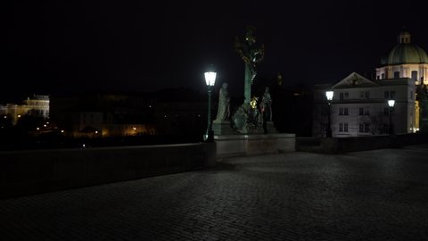 crossing of a street lighting lamp and an illuminated sculpture of St. Crosses with Calvary from the 18th century on a stone tower on Charles Bridge over the Vltava River in the center of Prague 
