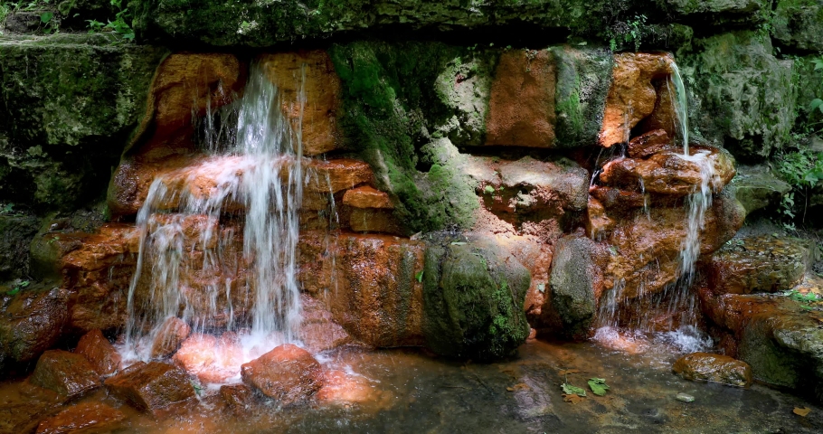A natural flow of water gushes forth from the colorful orange yellow rocks of the Yellow Spring at Glen Helen Nature Preserve in Greene County, Ohio in this seamless video loop