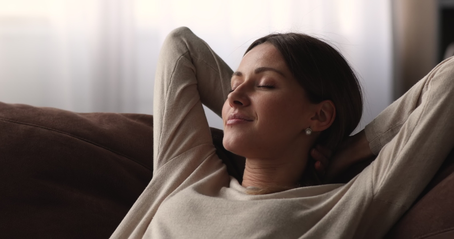 Close up head shot smiling young attractive caucasian woman daydreaming on cozy sofa with folded hands behind head, enjoying peaceful weekend moment alone in living room, lazy weekend pastime. Royalty-Free Stock Footage #1068565439