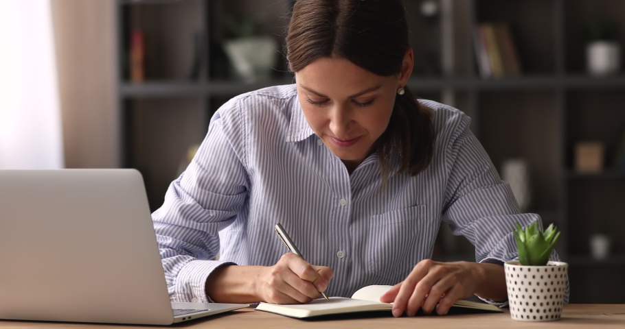 Happy young business lady handwriting in paper notebook, planning workday or meeting schedule, writing appointments or important information, creating wishes or making to-do list at home office. Royalty-Free Stock Footage #1068565601