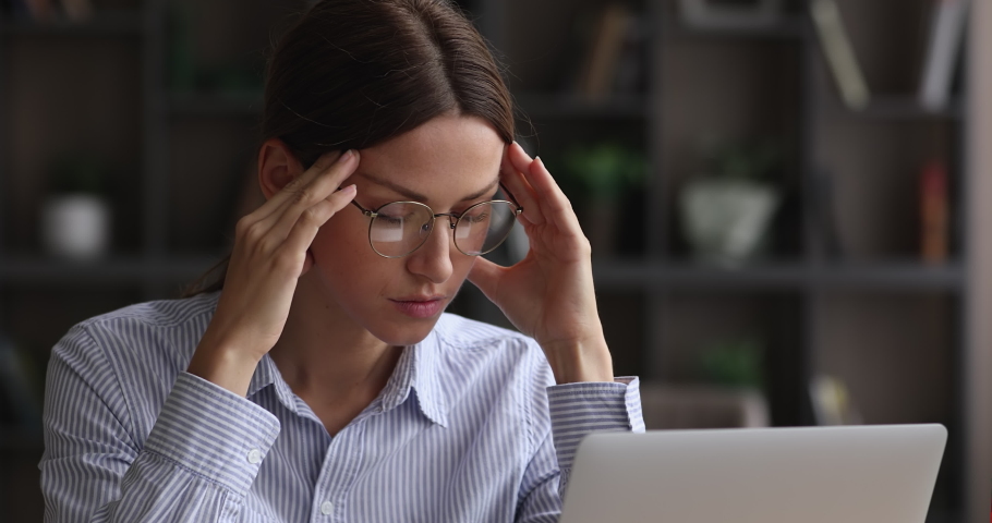 Close up head shot stressed overwhelmed young caucasian businesswoman in eyeglasses massaging temples, feeling exhausted, suffering from headache due to computer overwork, workaholic people concept. Royalty-Free Stock Footage #1068565637