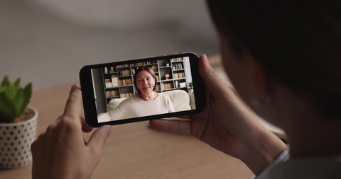 Close up focus on phone screen, young woman communicating with middle aged older retired mother using mobile video call zoom application, enjoying pleasant conversation, talking distantly online.