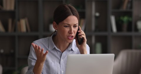 Stressed unhappy young woman holding unpleasant telephone conversation, working on computer in office, complaining about bad service work or feeling frustrated of professional business failure.
