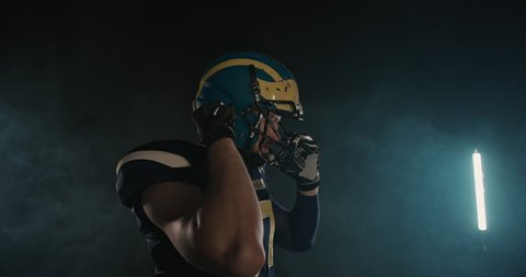 American football sportsman player putting on and tightening his football helmet on black background. Getting ready for game