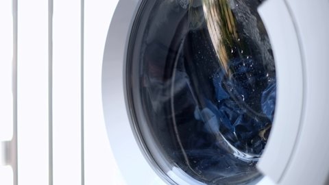 the laundry is washed in a white automatic washing machine behind a glass door, the metal drum rotates in different directions in turn. washing clothes jeans. homework 4k