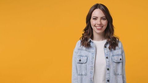 Surprised excited young woman 20s in denim jacket white t-shirt isolated on yellow background studio. People lifestyle concept. Pointing index finger aside up say wow showing thumbs up like gesture