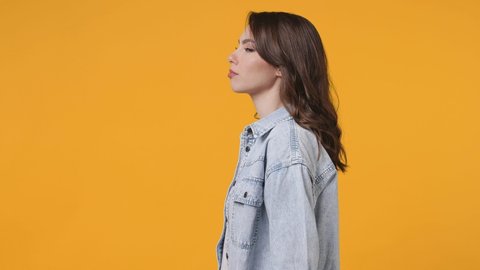 Side view of surprised amazed young woman 20s in denim jacket isolated on yellow background studio. People lifestyle concept. Turns around camera say wow omg cover mouth showing thumbs up like gesture