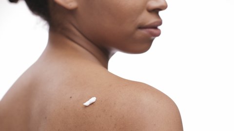 Close up shot of young african american lady applying moisturizing cream on her shoulder skin, back view, slow motion