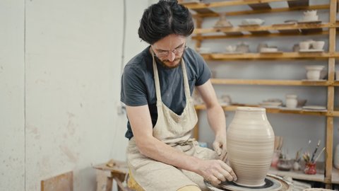 Pottery workshop. Focused man artist creating handmade ceramic vase on pottery wheel, tracking shot, slow motion