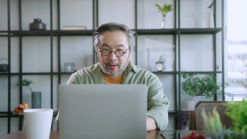 Silver hair and beard Male dad businessman freelancer working at home behind a laptop with super busy communication smarthpone calling. Remote work and family. | Shutterstock HD Video #1068591158