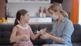 Mother wearing a medical mask is wearing a medical mask to her little daughter. Stay home, mom. Coronavirus or COVID-19. The mother teaches her daughter to wear a medical mask. Slow motion video.