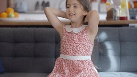 A beautiful girl with little long hair is sitting on an armchair in her home and playing with the hair. Portrait of beautiful little girl with long hair.Slow motion video.