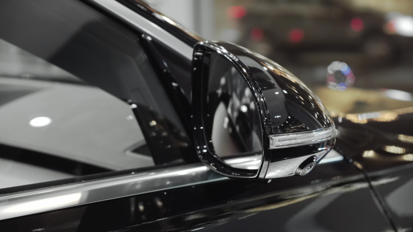 Folding and unfolding the outside rearview mirror with built-in turn signal light on a prestigious black car in a dealer showroom. Closeup cinematic 4k shot.