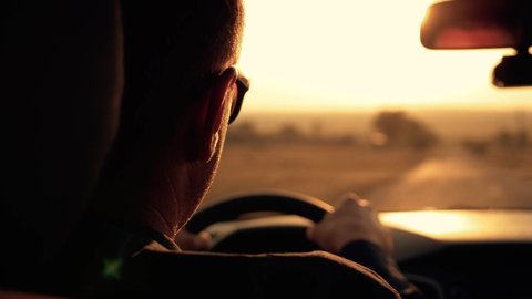 Male businessman drives a car while traveling. Man's hands lie on the steering wheel in the rays of the sunset. Silhouette of a man driving a car. Business, travel concept.