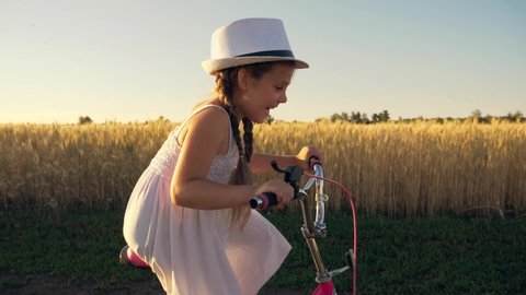 Girl cyclist in park leads an active lifestyle outdoors. Kid dreams of traveling by bike. Child rides a bicycle on road in the field. Girl in the park in nature rides a bicycle on the grass