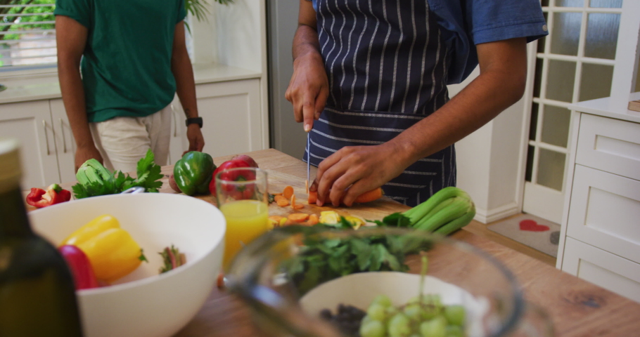 Happy mixed race gay male couple hugging while preparing food in kitchen. staying at home in isolation during quarantine lockdown.