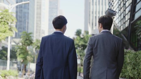 rear view of two asian business men talking walking in downtown of modern city