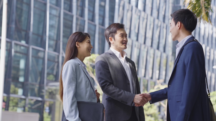 Asian business associates shaking hands and talking in the street in downtown of modern city