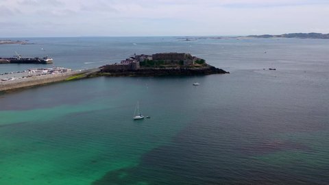 Panoramic view across Havelet Bay St Peter Port Guernsey, Castle Cornet and the Little Russell Channel to Herm on a calm sunny summer day with clear turquoise sea and yacht at anchor.