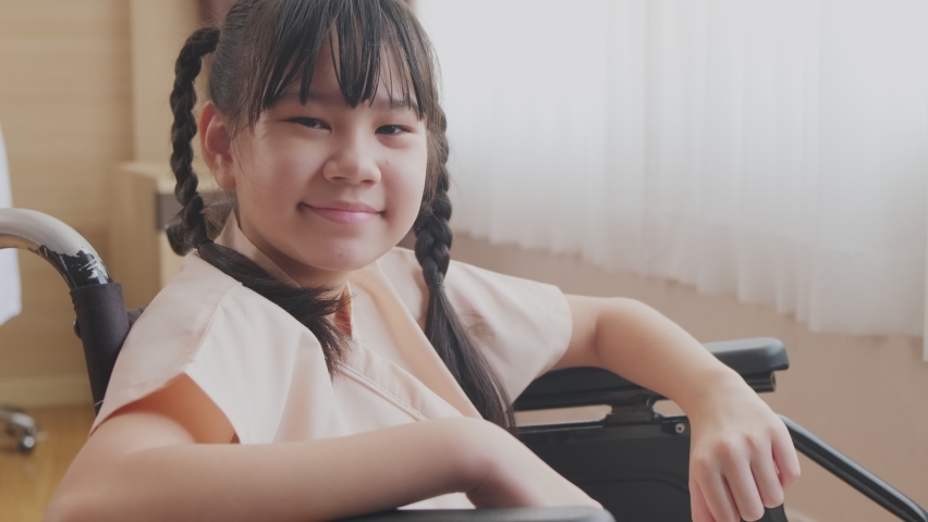 Portrait of Asian little illness girl sitting on wheelchair with smiling in hospital while waiting for medical service. The young kid feeling good, hopeful and thumbs up with cheerful and happy face.