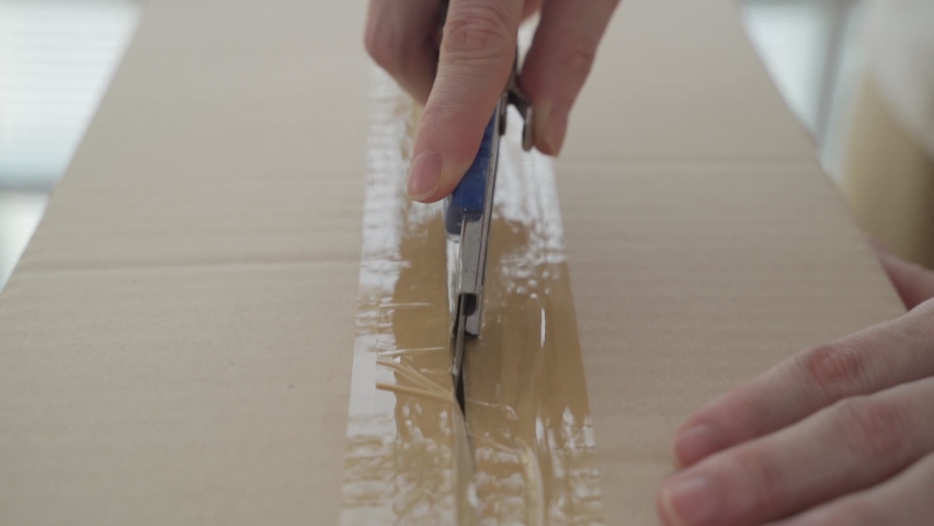 female hand using sharp cutter knife slashing tape on cardboard box to open carton parcel.  Royalty-Free Stock Footage #1068623990