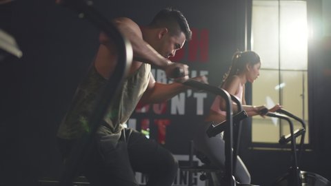 Close-up shot of people sitting on stationary bicycles or exercise bikes in stadium. Asian muscle man and woman spinning on cardio machine together. Health care and fitness in gym concept.