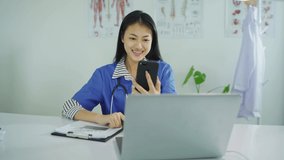 Asian Beautiful woman doctor Sitting at a desk, using a smartphone, video calling with patients online. In the clinic office at work time