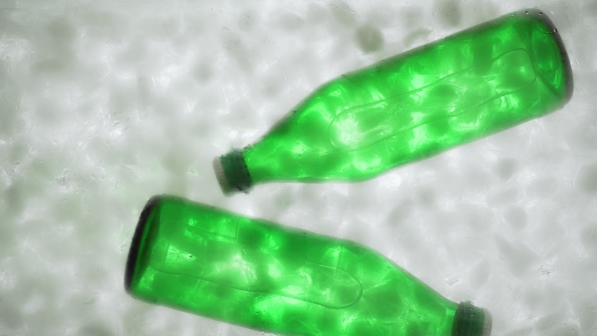 Hands put two green bottles of water or soda in a container with ice, bottom view. Water bottles in ice cubes.