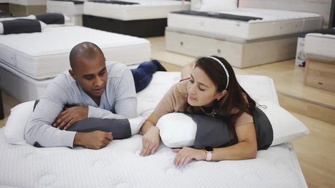 Man and woman choosing mattress in store trying it. High quality FullHD footage