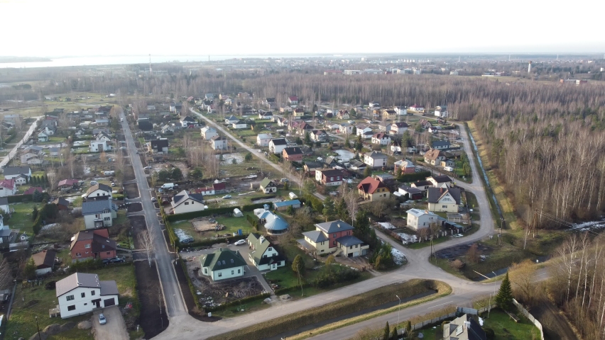 Drone fly over in Purvs area of Salaspils city in Latvia in winter (December 2020) without snow, with green grass showing, typical Latvian residential area with detached houses, forest and roads
