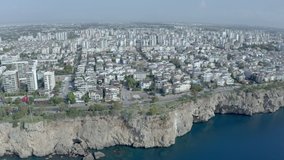 Drone video of the waterfront in the city on the Mediterranean Sea. Houses and streets overlook the rocky shoreline of the sea. Landscape place by the sea in Europe. Aerial view Antalya Turkey.