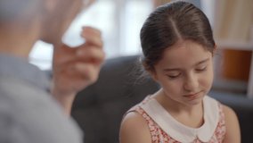 A beautiful girl with little long hair sits in an armchair and is bored. Close-up portrait of thoughtful and sad little girl. Slow motion video.