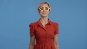 Great offer. Surprised woman screaming and lowering her glasses, Blue studio background. The woman is wearing glasses and a red dress. Slow motion video.